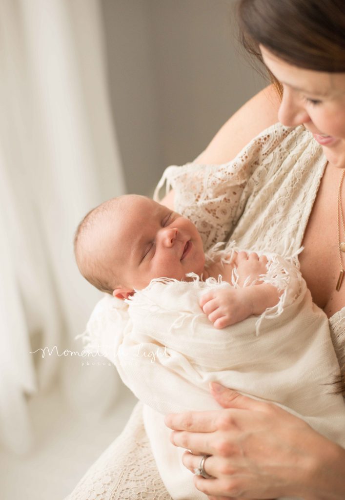 mom holding newborn baby while baby smiles