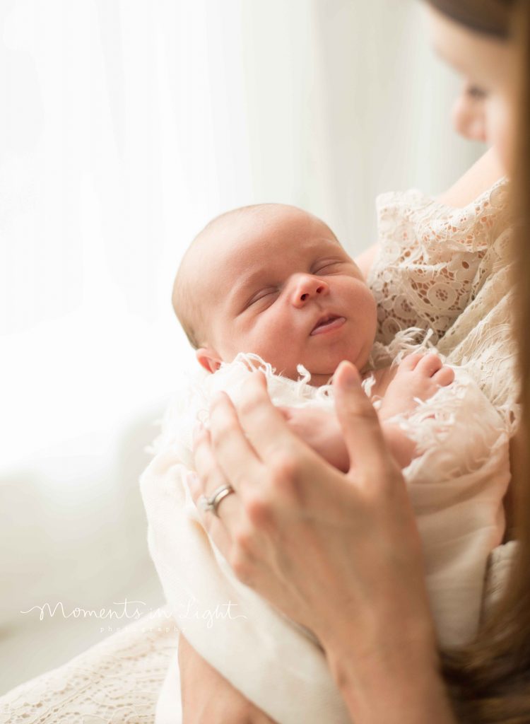 closeup of mother holding newborn baby by window