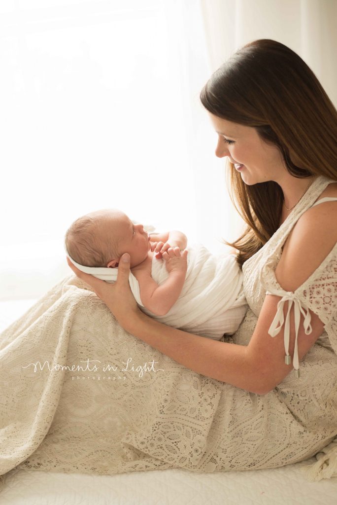 mom in cream lace dress holding her newborn baby on bed