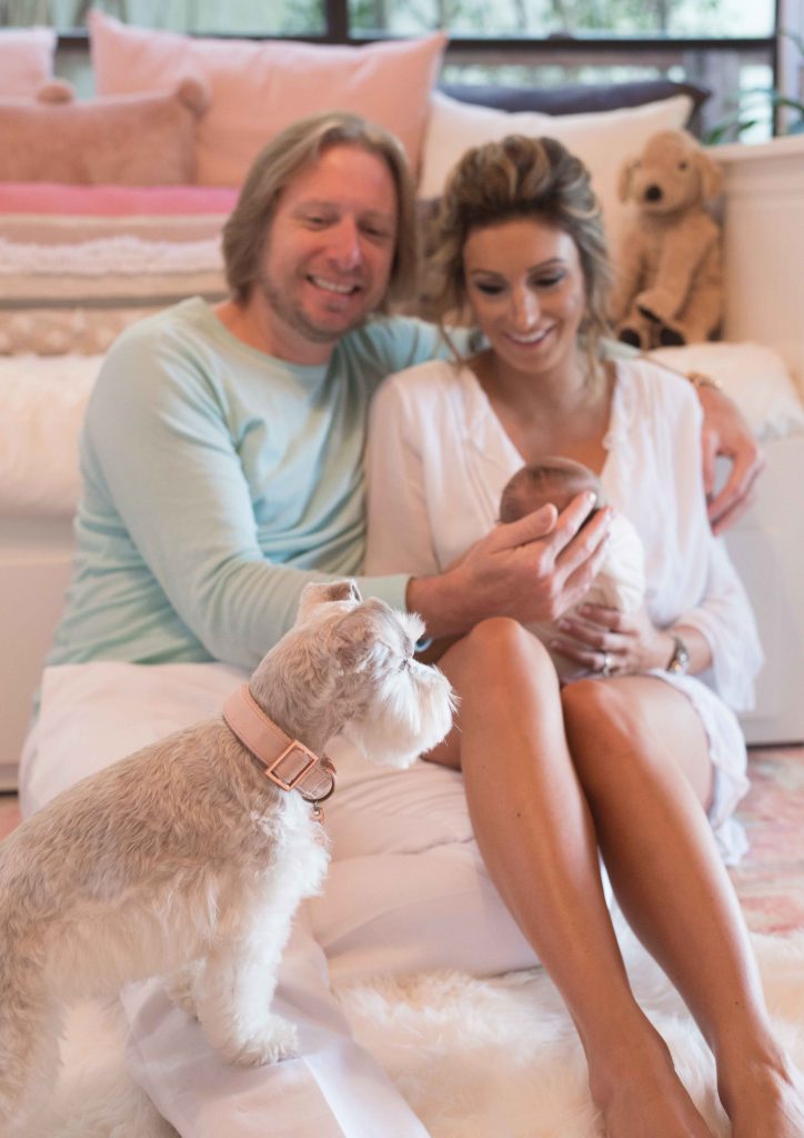 mom and dad sitting in nursery holding newborn baby with dog looking