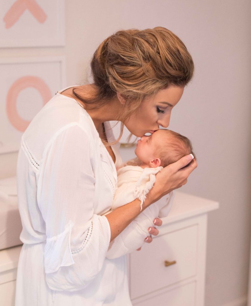 mom kissing newborn baby's head in nursery