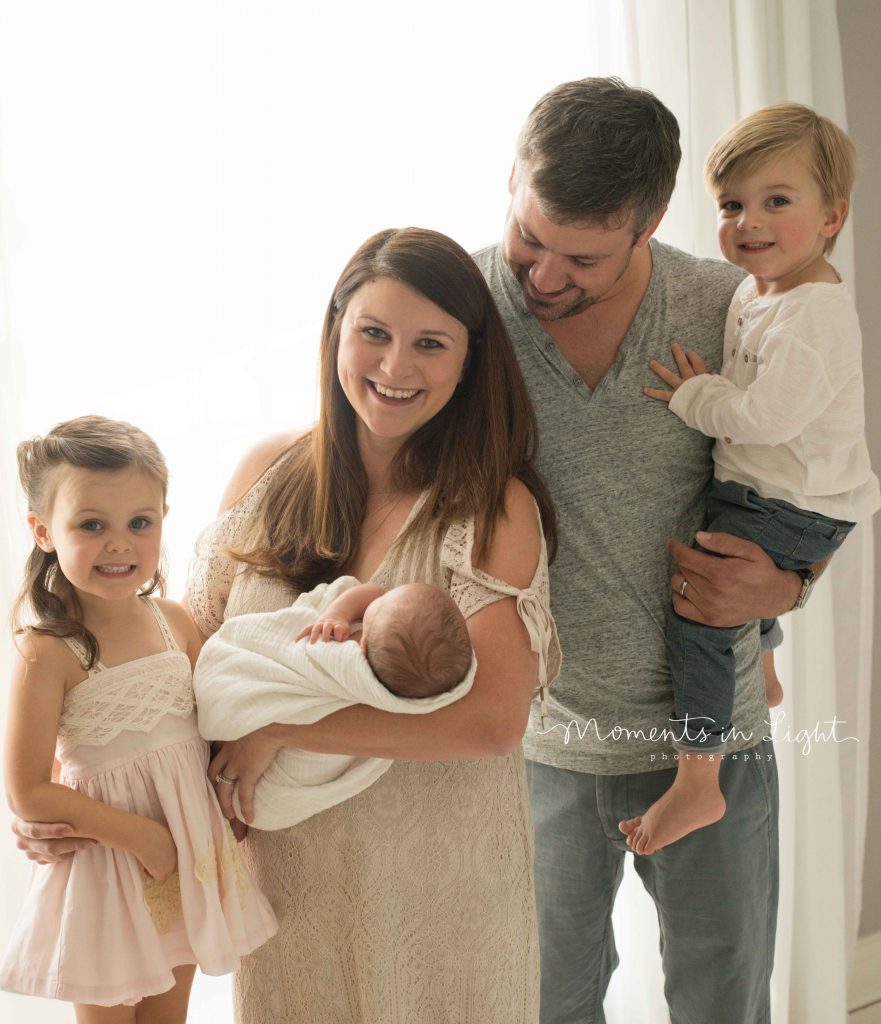 family with toddlers and newborn baby standing by window