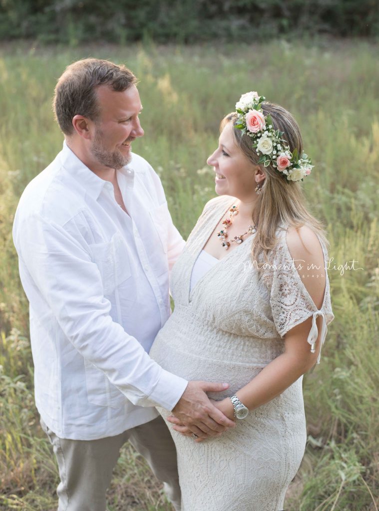 maternity photo of woman in a lace dress with a floral crown in a field in The Woodlands, TX with husband