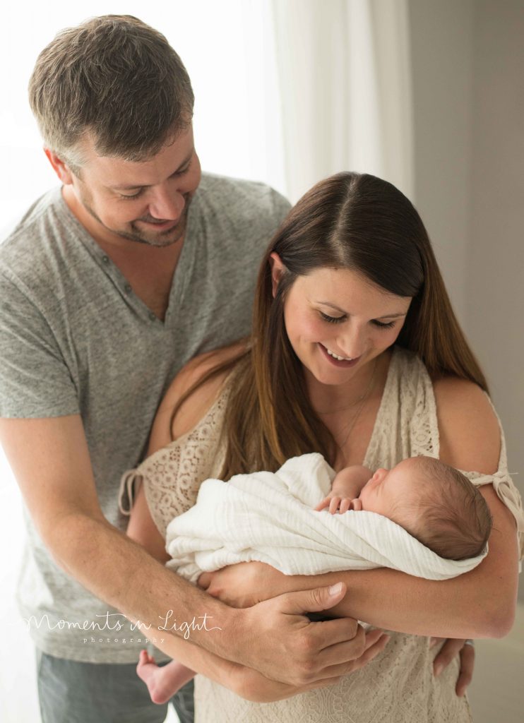 mom and dad holding newborn baby smiling down at baby