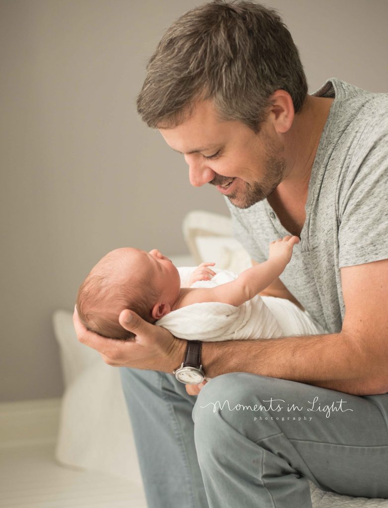 dad holding newborn baby smiling down at baby