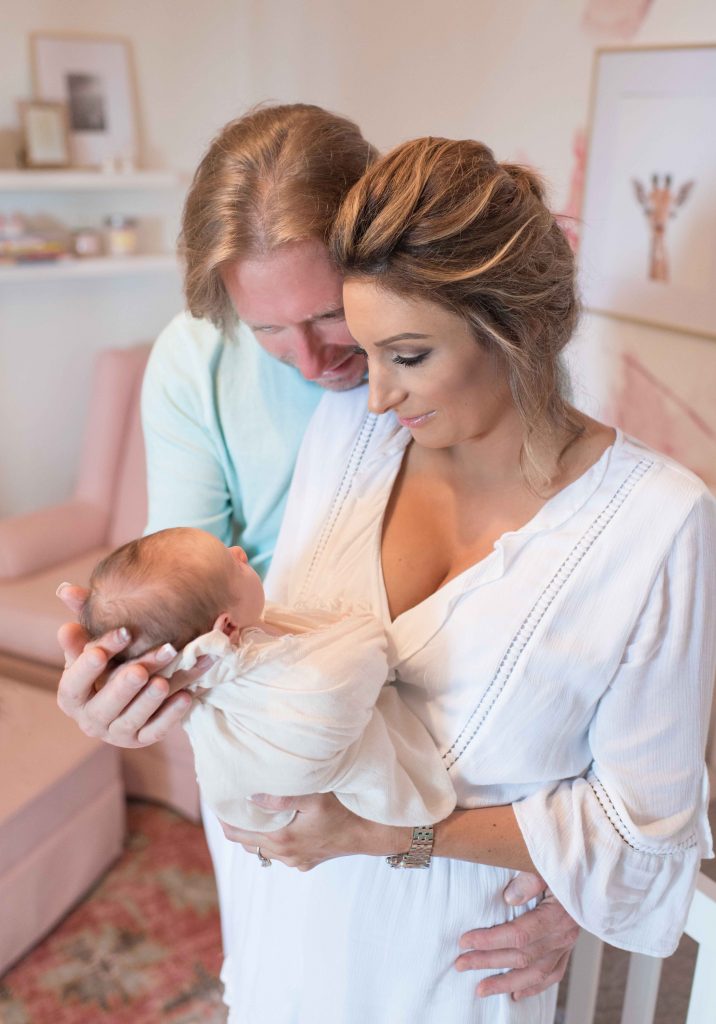 mom and dad holding and looking at newborn baby in nursery