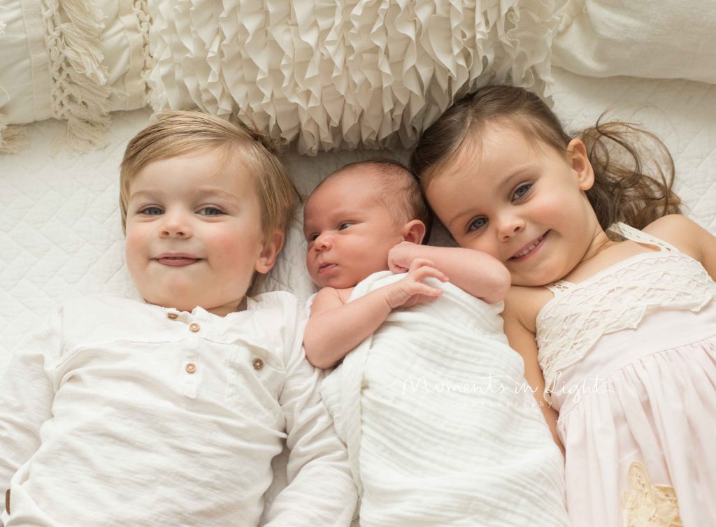 siblings with newborn baby laying on bed 