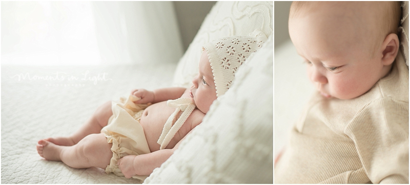 A baby with a big belly and lace bonnet lays on a white bed. 