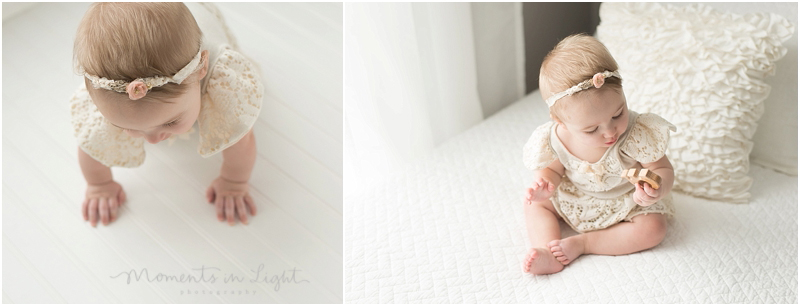 A baby girl sits on a white bed and plays with a toy that grabs her attention. 