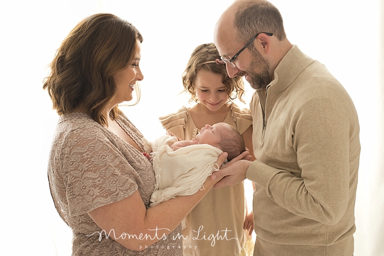 Mother, Father and older sister smiling at newborn boy in photography studio in The Woodlands