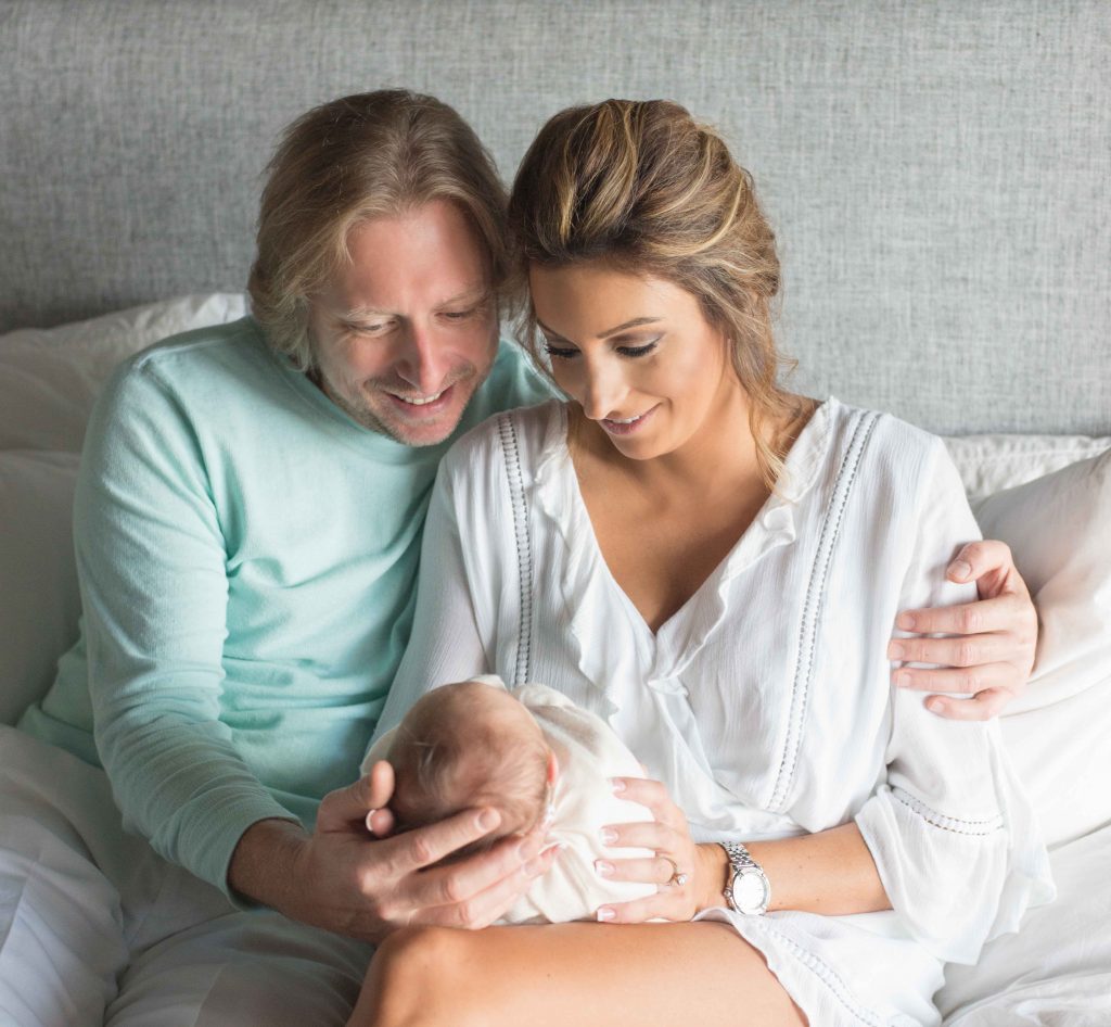 mom and dad holding newborn baby and smiling on bed