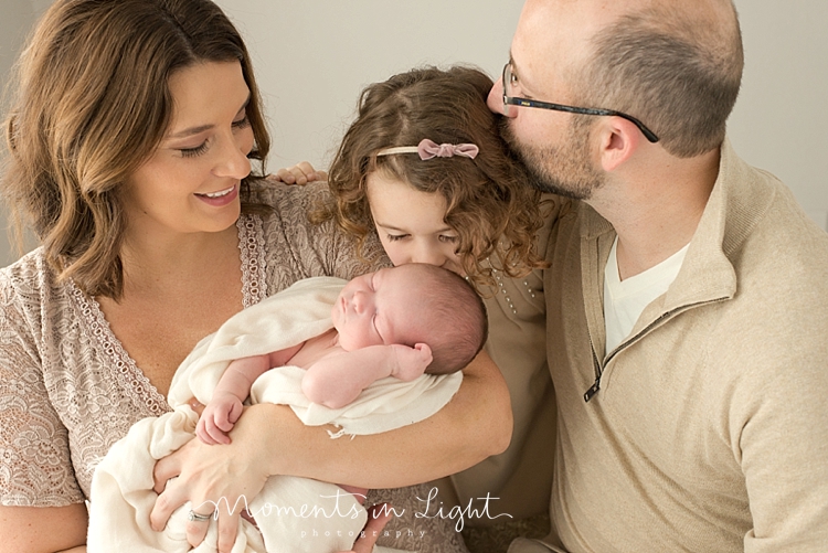 Big sister kissing newborn brother's head with both parents smiling in Houston photography studio