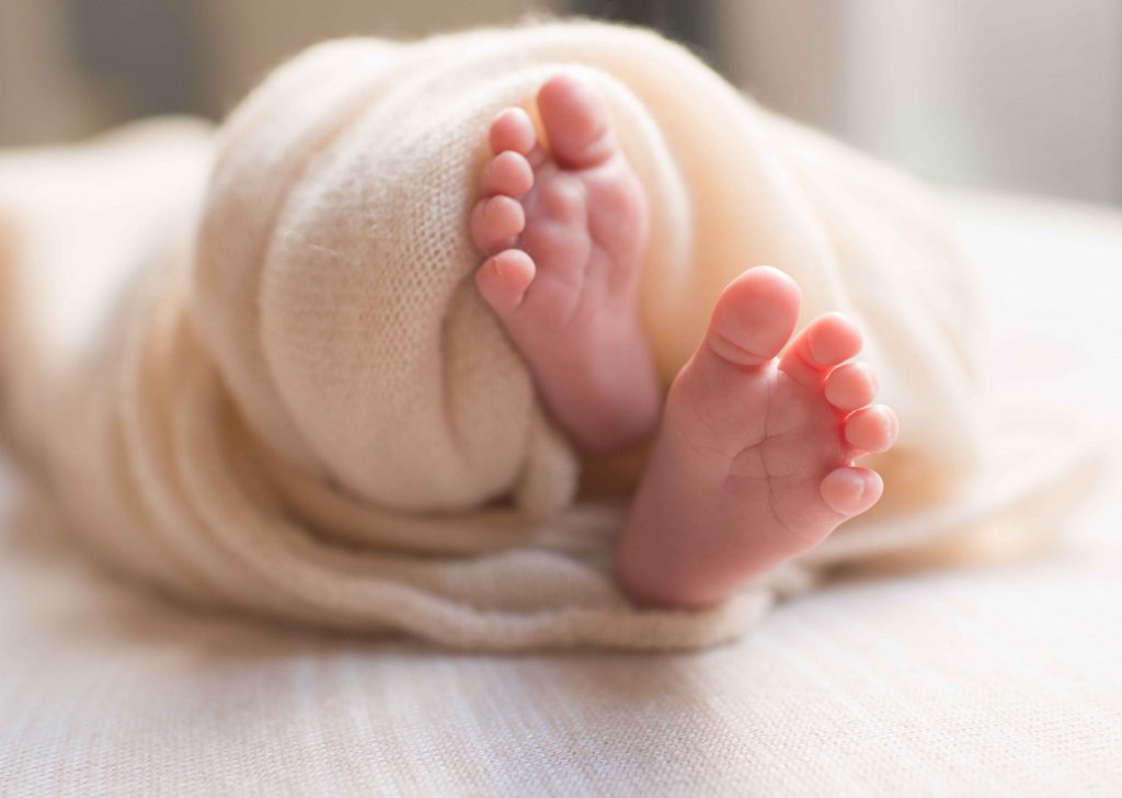 close up of newborn baby feet wrapped in knit cream blanket