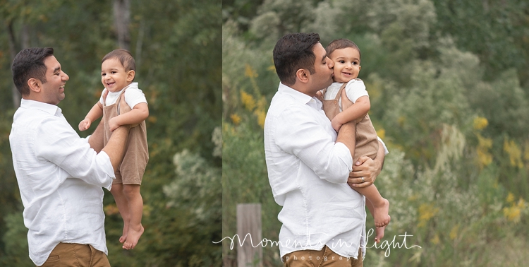 Father holding and kissing baby boy  in a field in The Woodlands