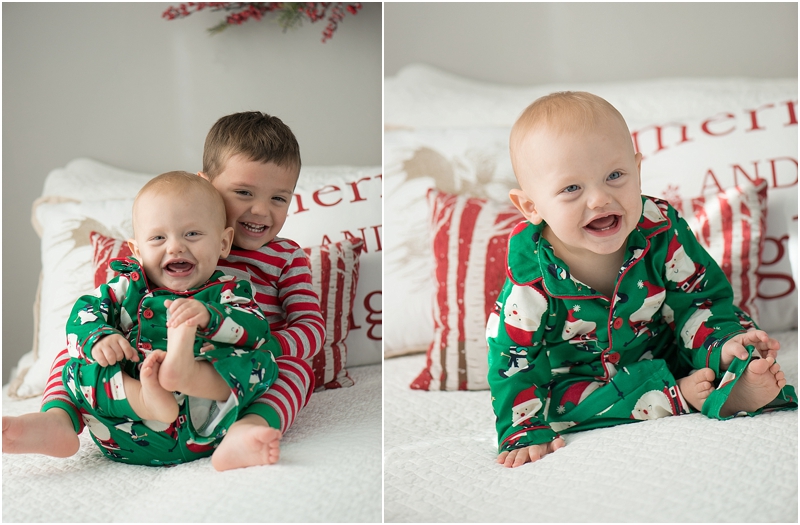 A boy holds his baby brother on a bed while wearing Christmas pajamas. 