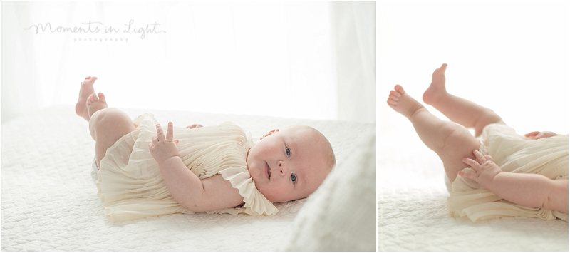 A baby kicks her chubby legs up in the air as she lays on a white bed. 