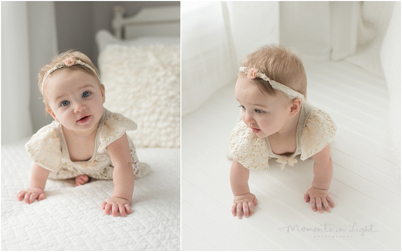 A baby wearing a flower headband crawls on a white bed. 