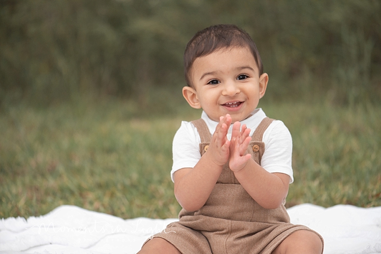 Baby boy wearing brown overalls clapping in a field by family photographer in Montgomery, Texas