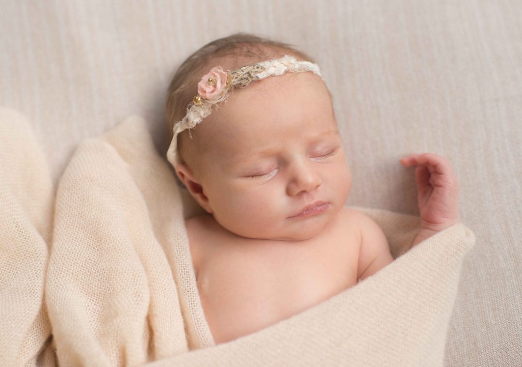 newborn baby girl with delicate floral cream headband and cream blanket