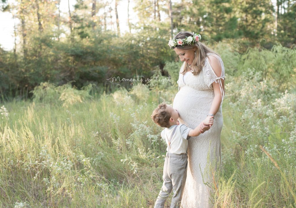 pregnant woman with young son kissing belly in field in The Woodlands, TX