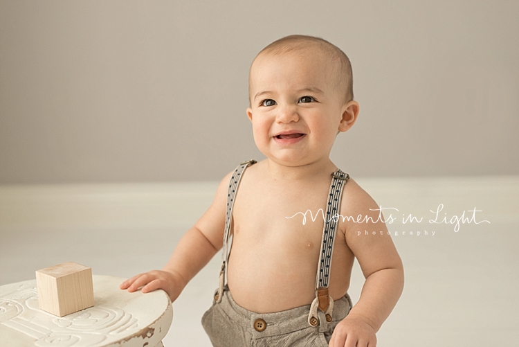 Young boy in suspenders playing with wooden block in Houston baby photography studio