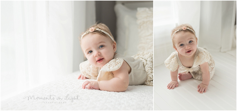 A baby with blue eyes lays on her belly on a white bed. 