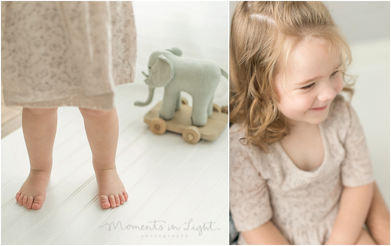 A wooden elephant toy sits near a girl with a lace dress and bare feet. 