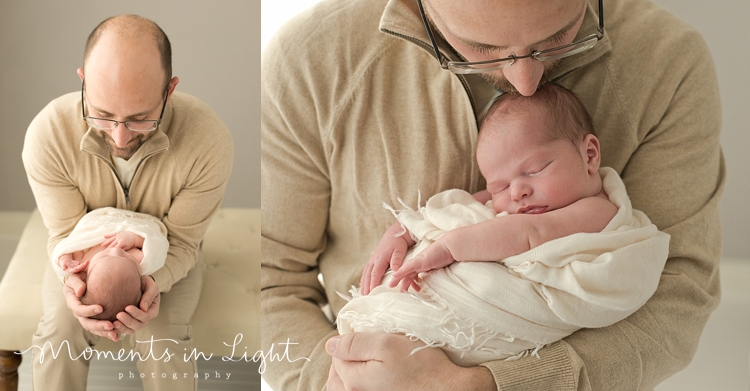 Father in a tan sweater smiling down at newborn baby in a Houston photography studio