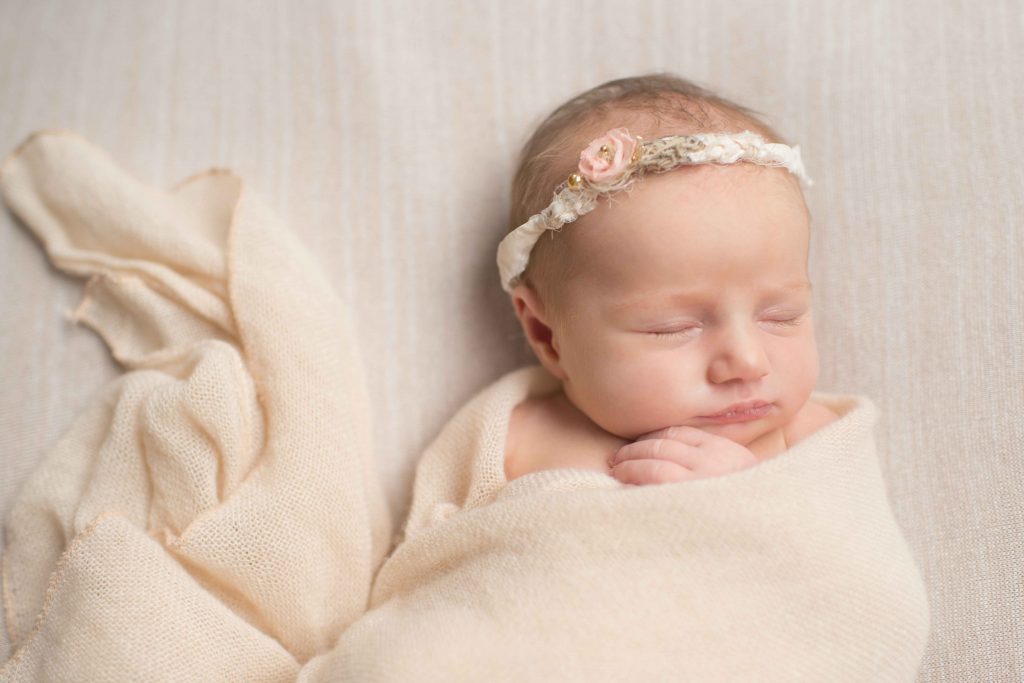 newborn baby girl in delicate floral headband and cream blanket wrap