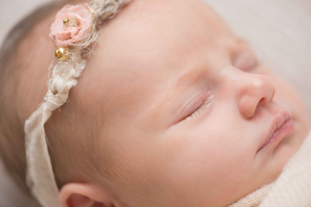 close up of newborn baby girl with long eyelashes wearing delicate floral headband