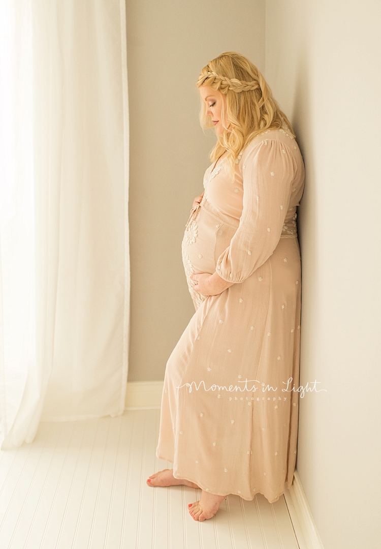 A pregnant woman leans against a wall and holds her belly. 