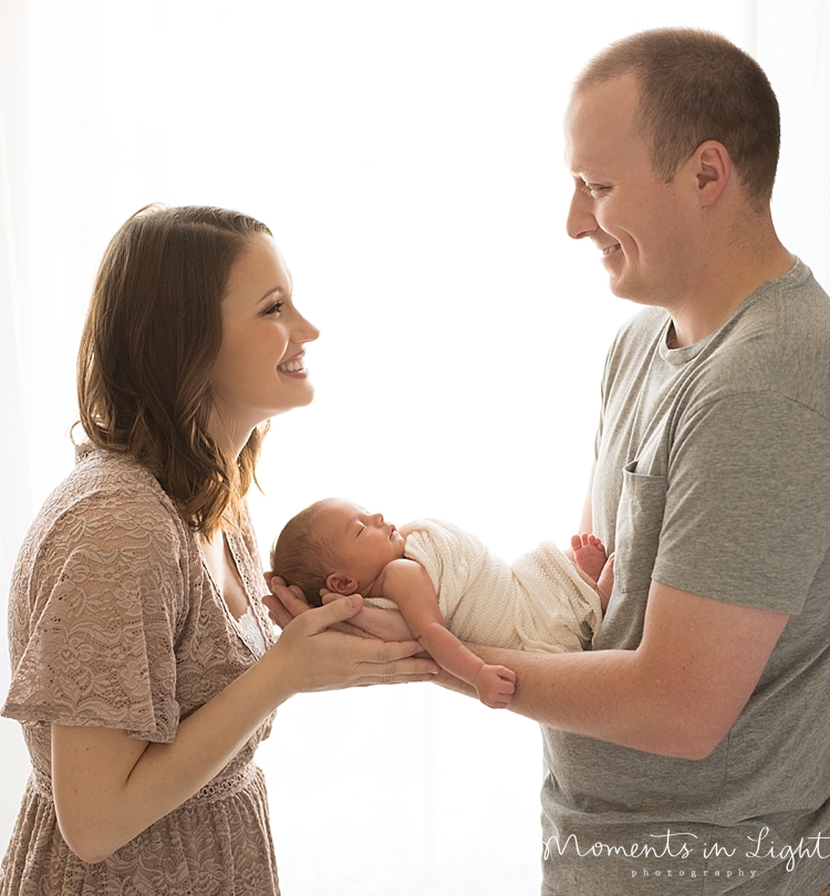 A man passes his newborn baby to her mother while smiling. 