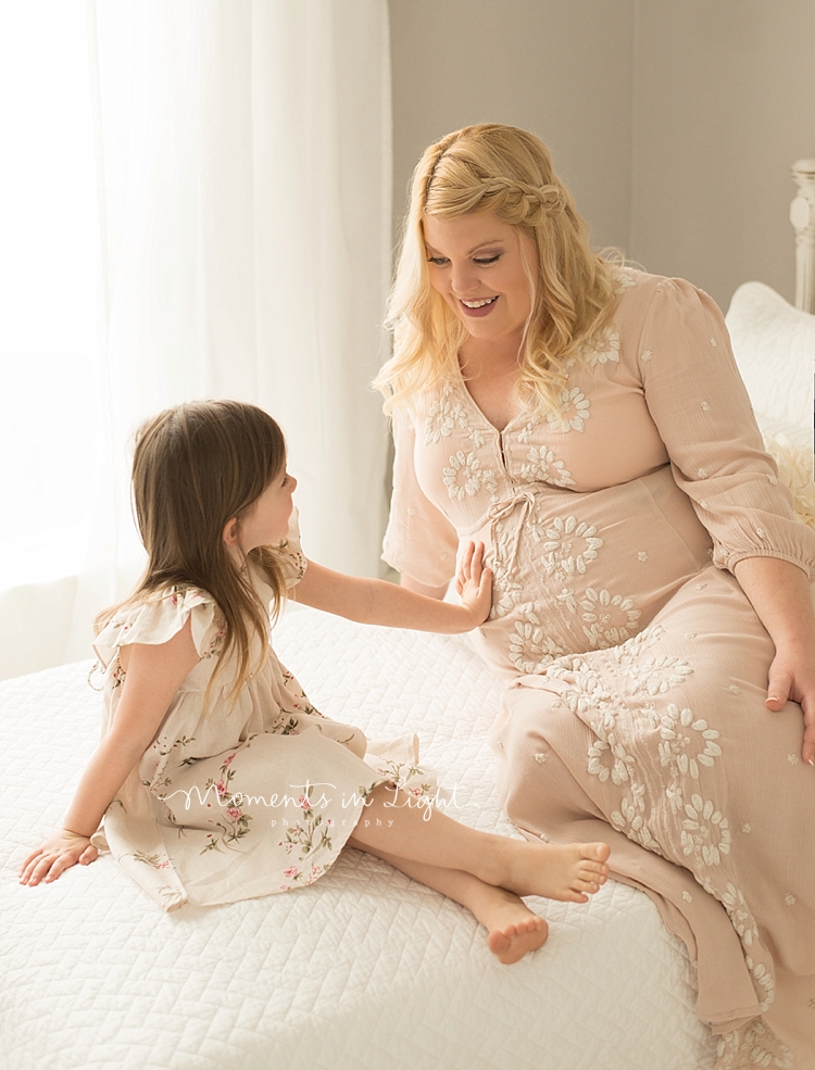 A little girl reaches out and touches her mom's pregnant belly. 