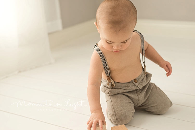 Baby boy in suspenders playing with wooden toys by baby photographer in The Woodlands