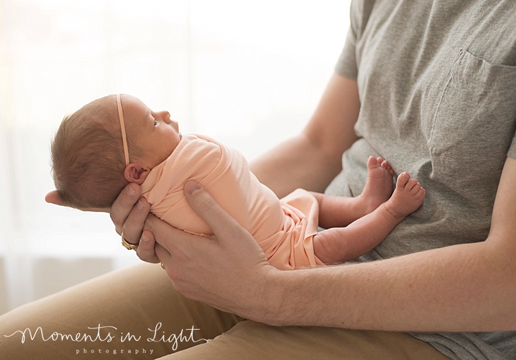 A man holds his newborn daughter with his hands on his lap while she sleeps. 