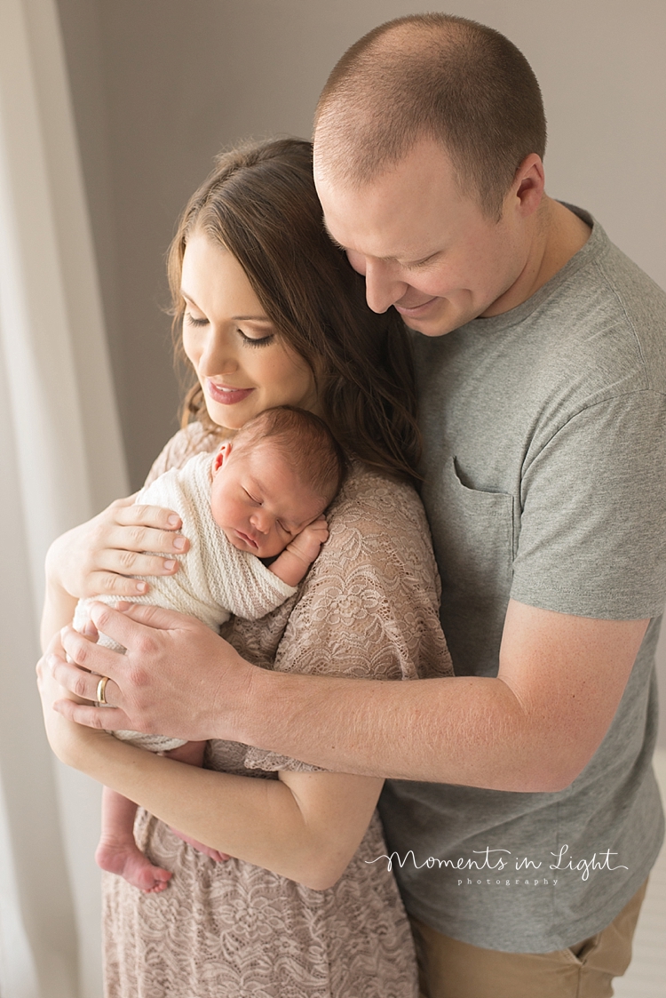 A man hugs his wife as she holds their newborn daughter. 