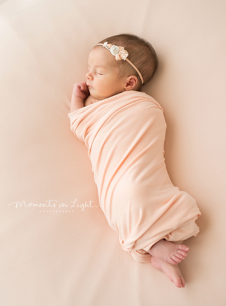 A newborn naps while wearing a flower headband. 