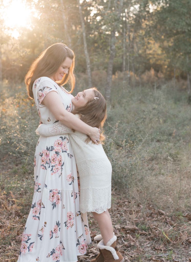 mom and daughter hugging with sunlight behind them in a field in The Woodlands, TX