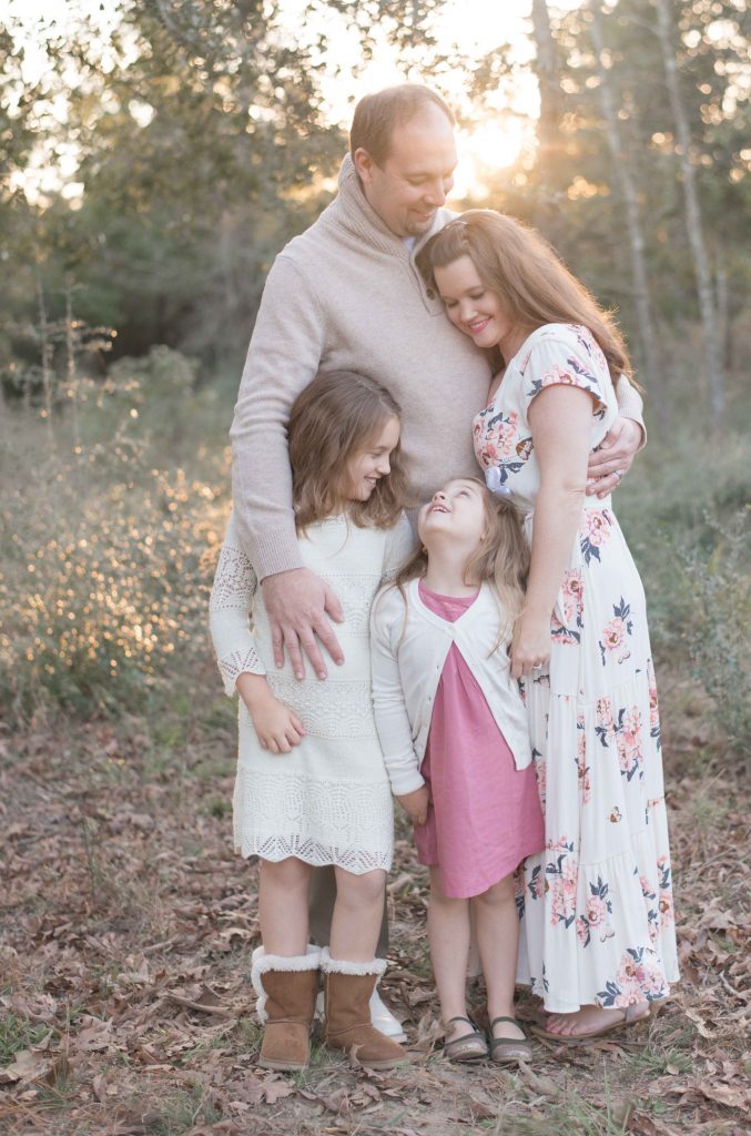 family of four hugging with sunset in a field in The Woodlands, TX