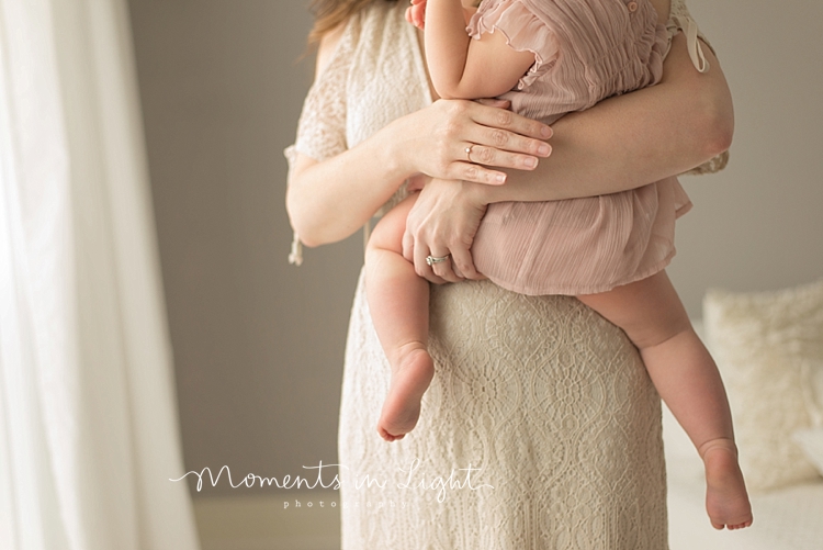 A mom holds her baby girl on her hip and supports her with her arm. 