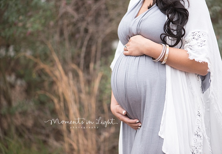 Some tall grass stands tall behind a pregnant belly. 