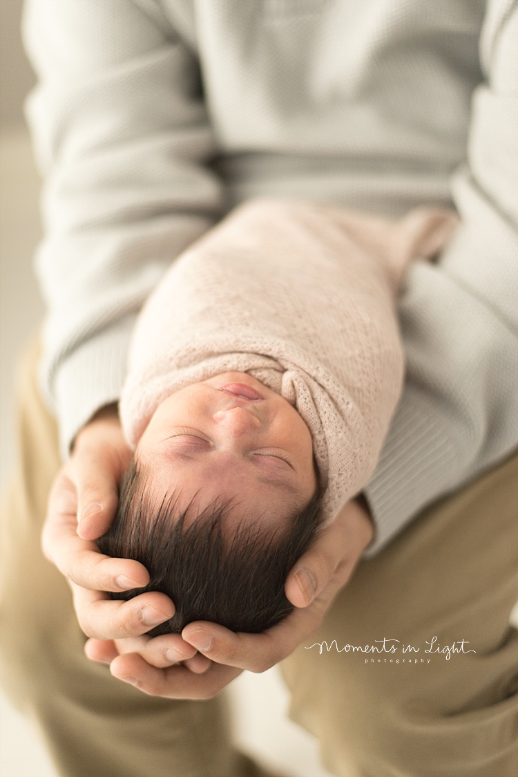 A baby girl newborn sleeps in dad's hands. 