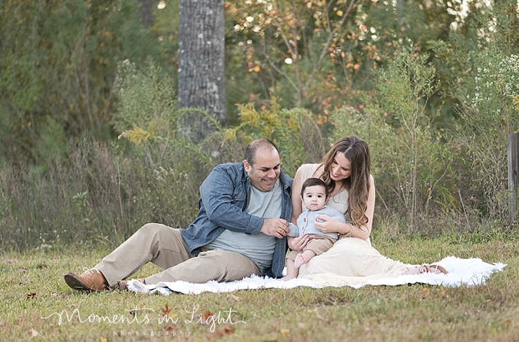 Two parents sitting with baby boy in a field by Montgomery, Texas family photographer