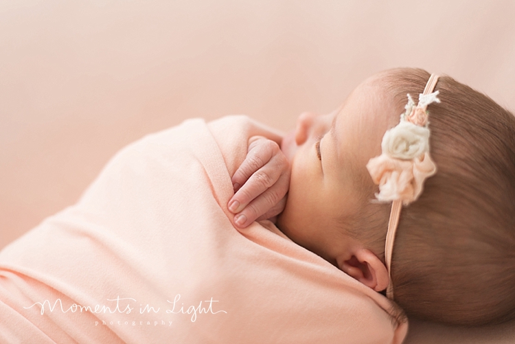 A newborn swaddled in a pink blanket naps with her hand peeking out. 