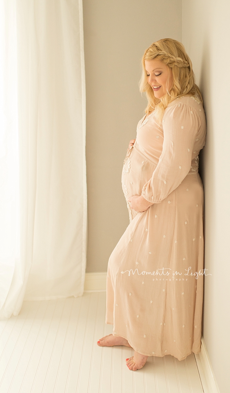 An expecting mother holds her belly while leaning against a wall. 