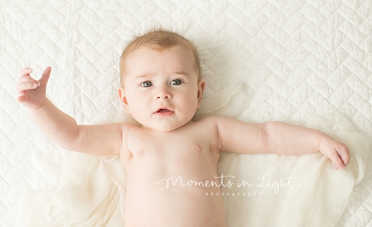 A baby stretches his arms out while laying on a blanket. 