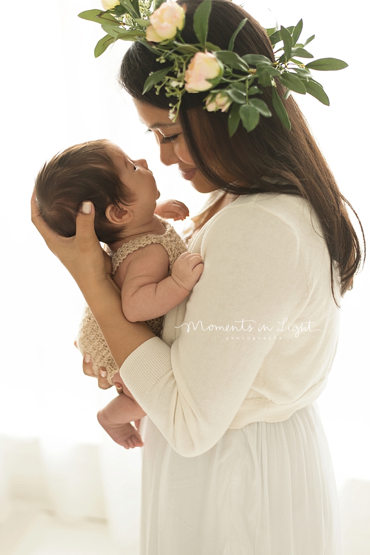 A mom wearing a flower crown holds her baby close to her face and smiles. 