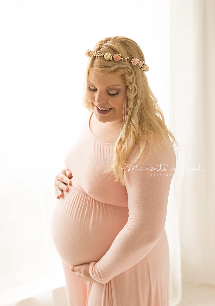 A woman with a flower crown and a pink dress holds her belly. 