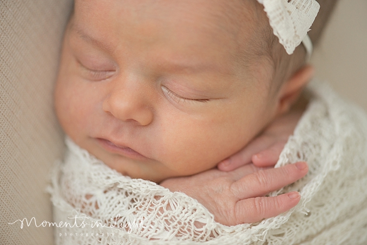 A newborn sleeps while wrapped in a white lace blanket. 