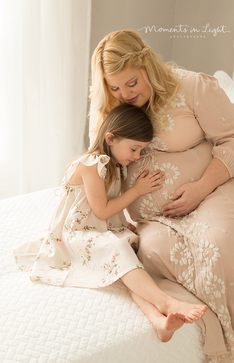 A mother hugs her daughter while she touches her pregnant belly. 